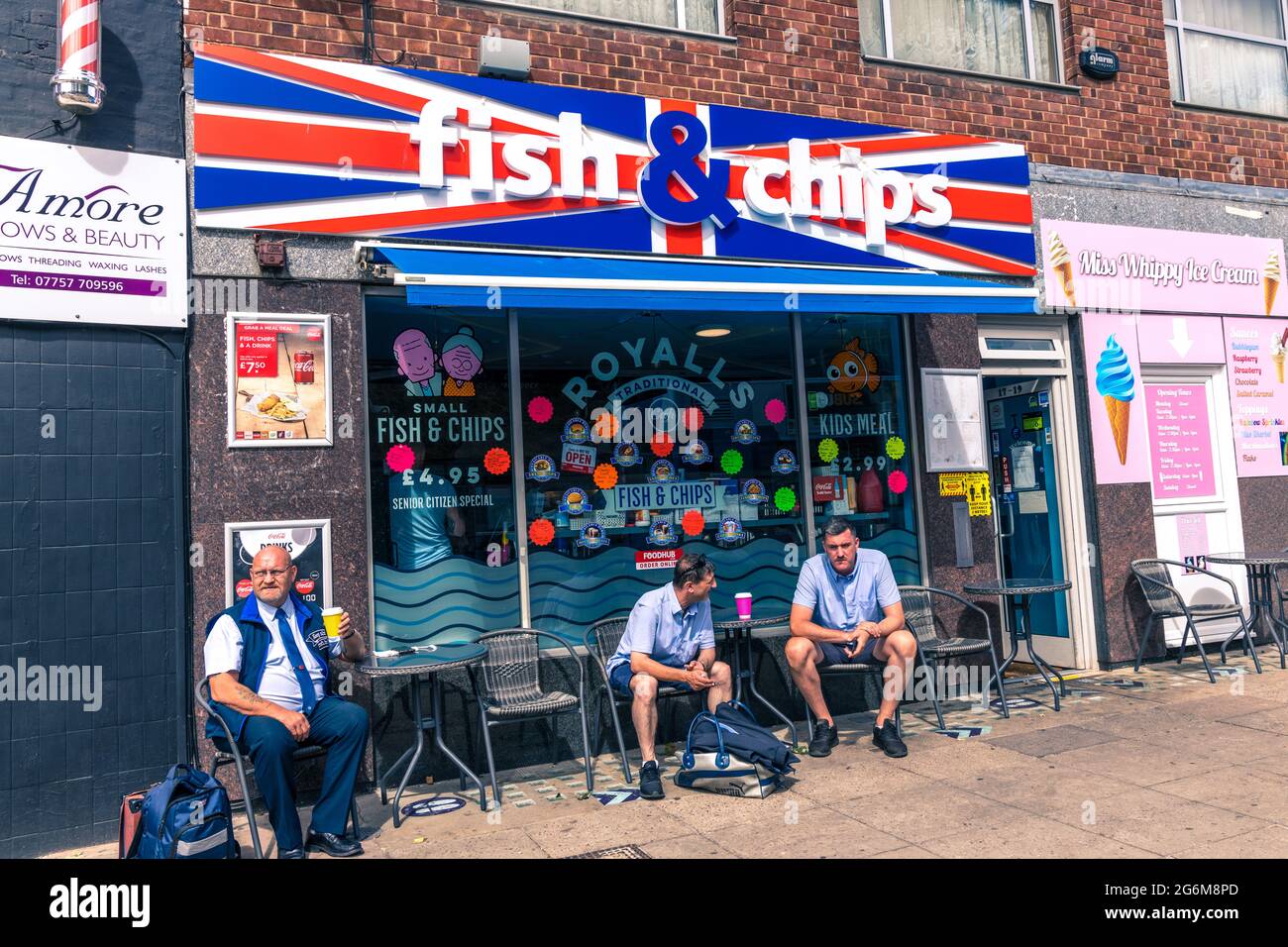 Three man sitting outside and typical British fish and chip shop which is decorated with the union flag Norwich England Stock Photo