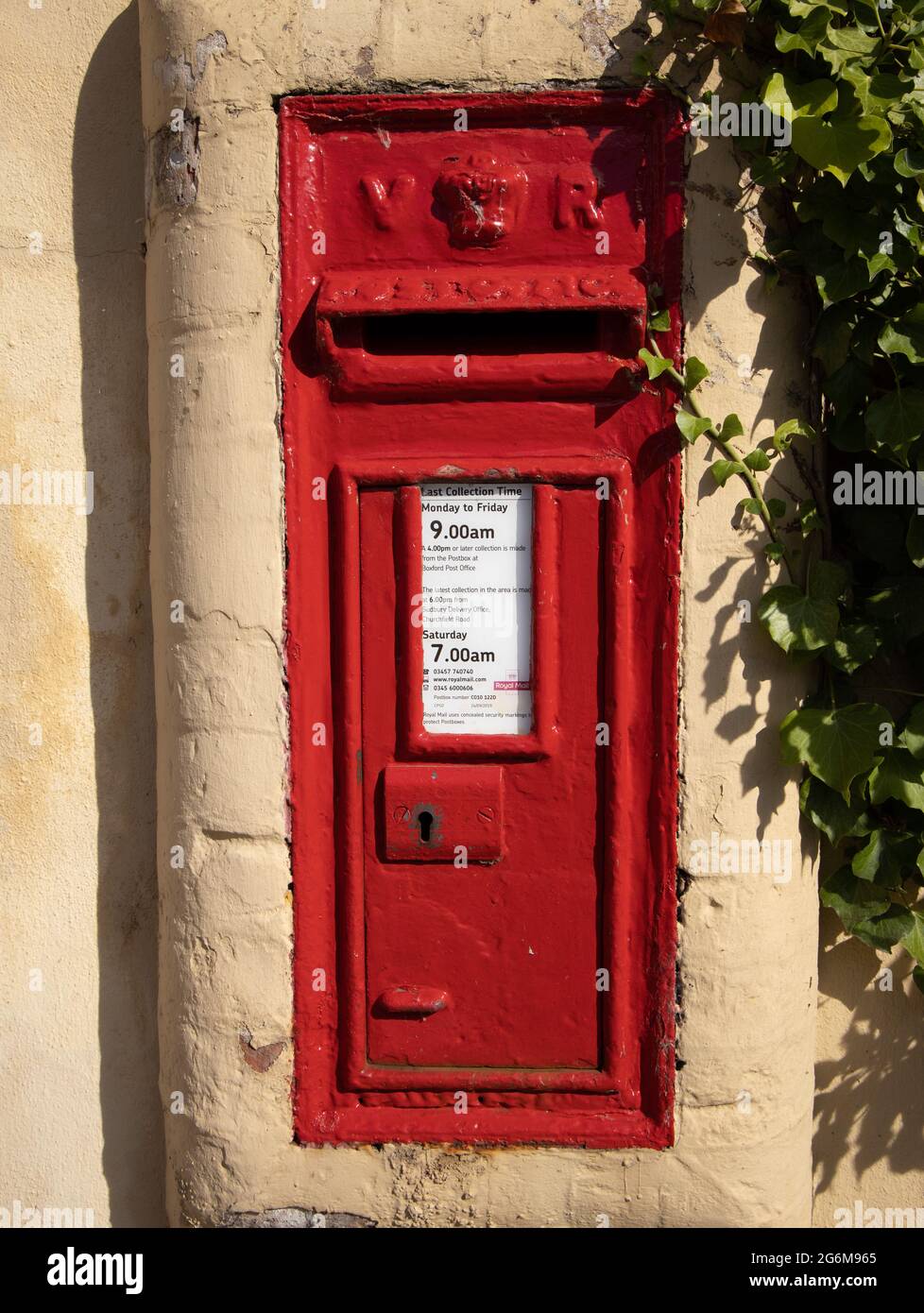 Red letter box built into a wall showing collection times England Stock Photo