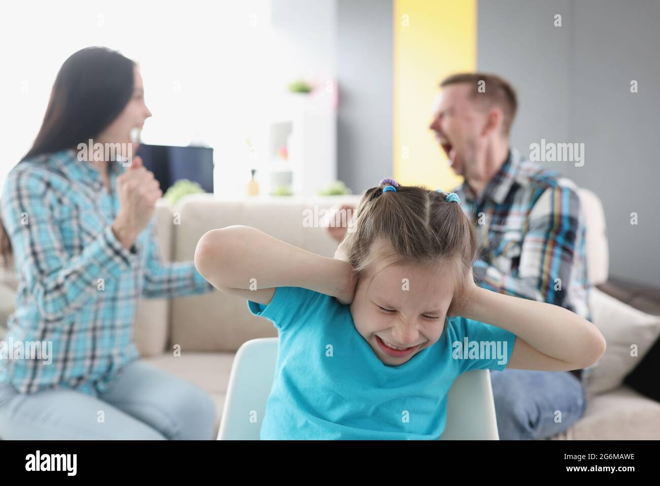Little girl closing her ears against background of swearing parents at home Stock Photo