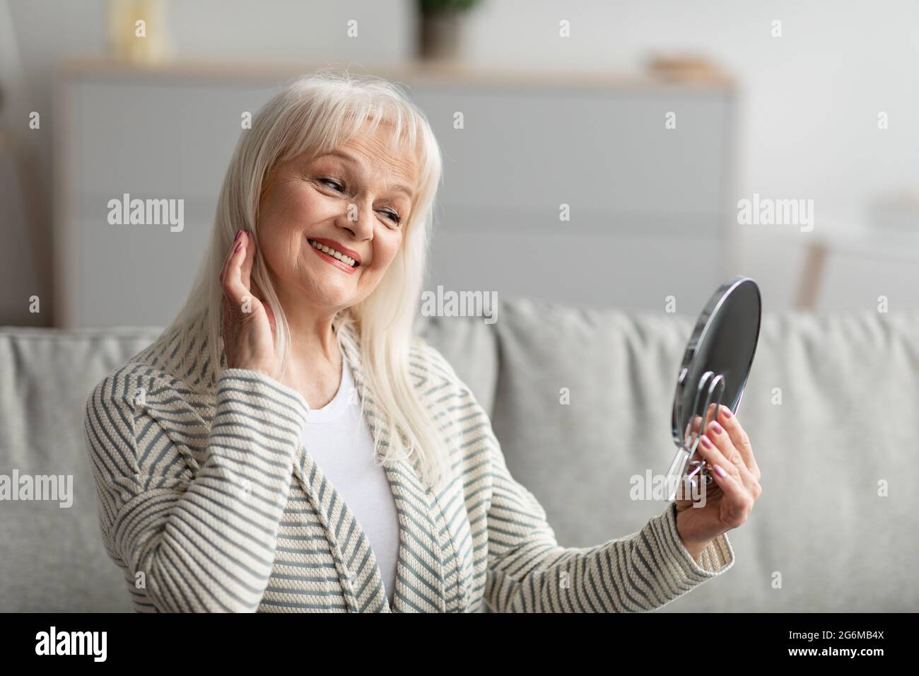 Smiling mature woman checking her face looking in mirror Stock Photo