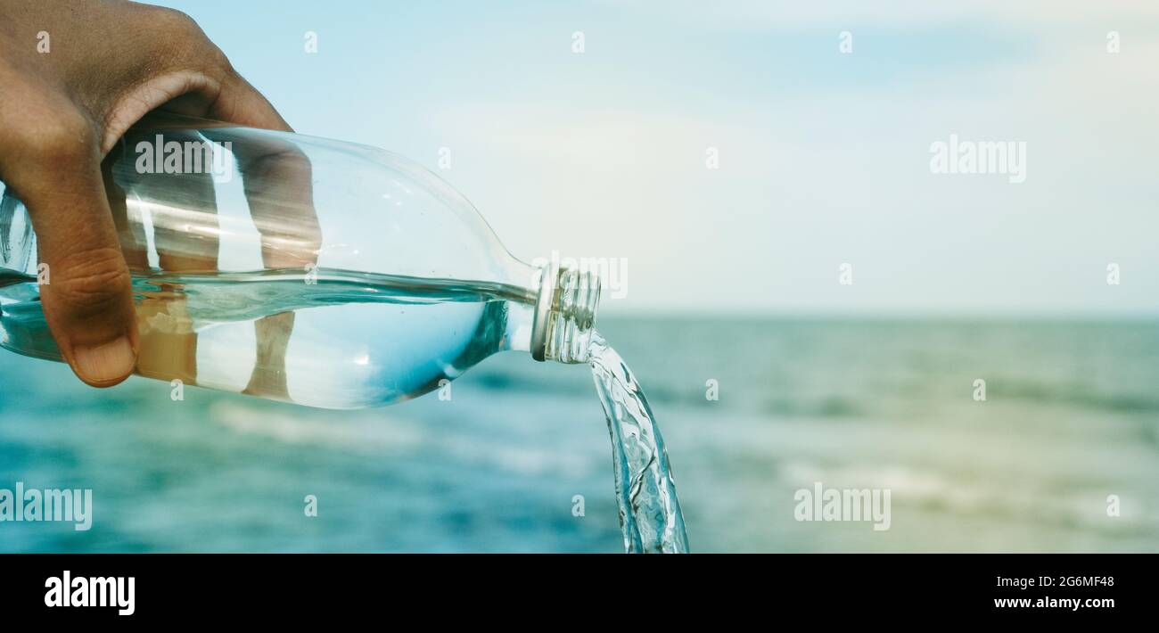 closeup of a young caucasian man pouring water from a reusable water bottle in front of the sea, in a panoramic format to use as web banner or header Stock Photo