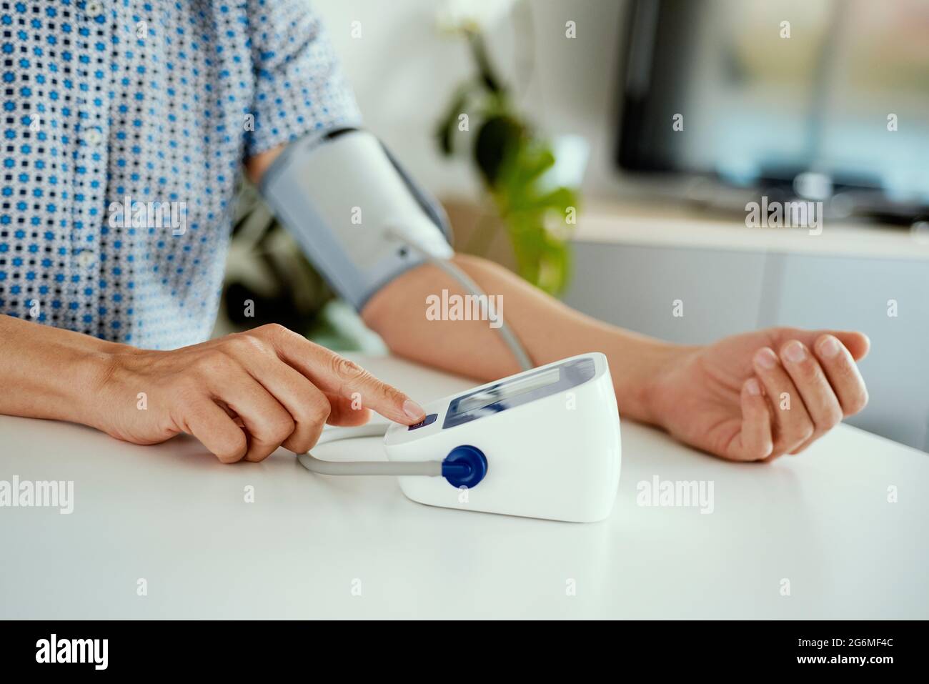 closeup of a caucasian man measurins his blood pressure with an electronic sphygmomanometer, sitting at a white table Stock Photo