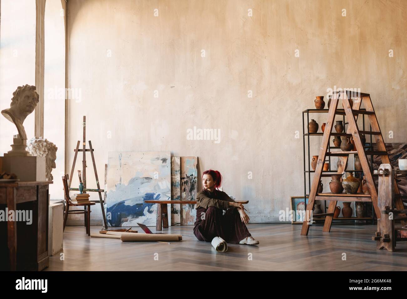 Young woman artist sitting on a floor of an art studio unrolling ...