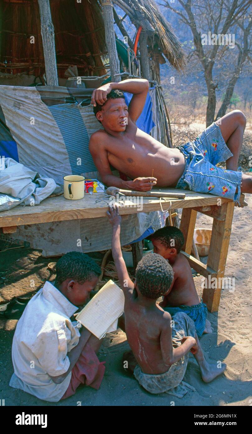Botswana: A bushmen camp with simple huts at Tsodillo Hills in the Central Kalahari where a bushmen and his children are realaxing and playing Stock Photo