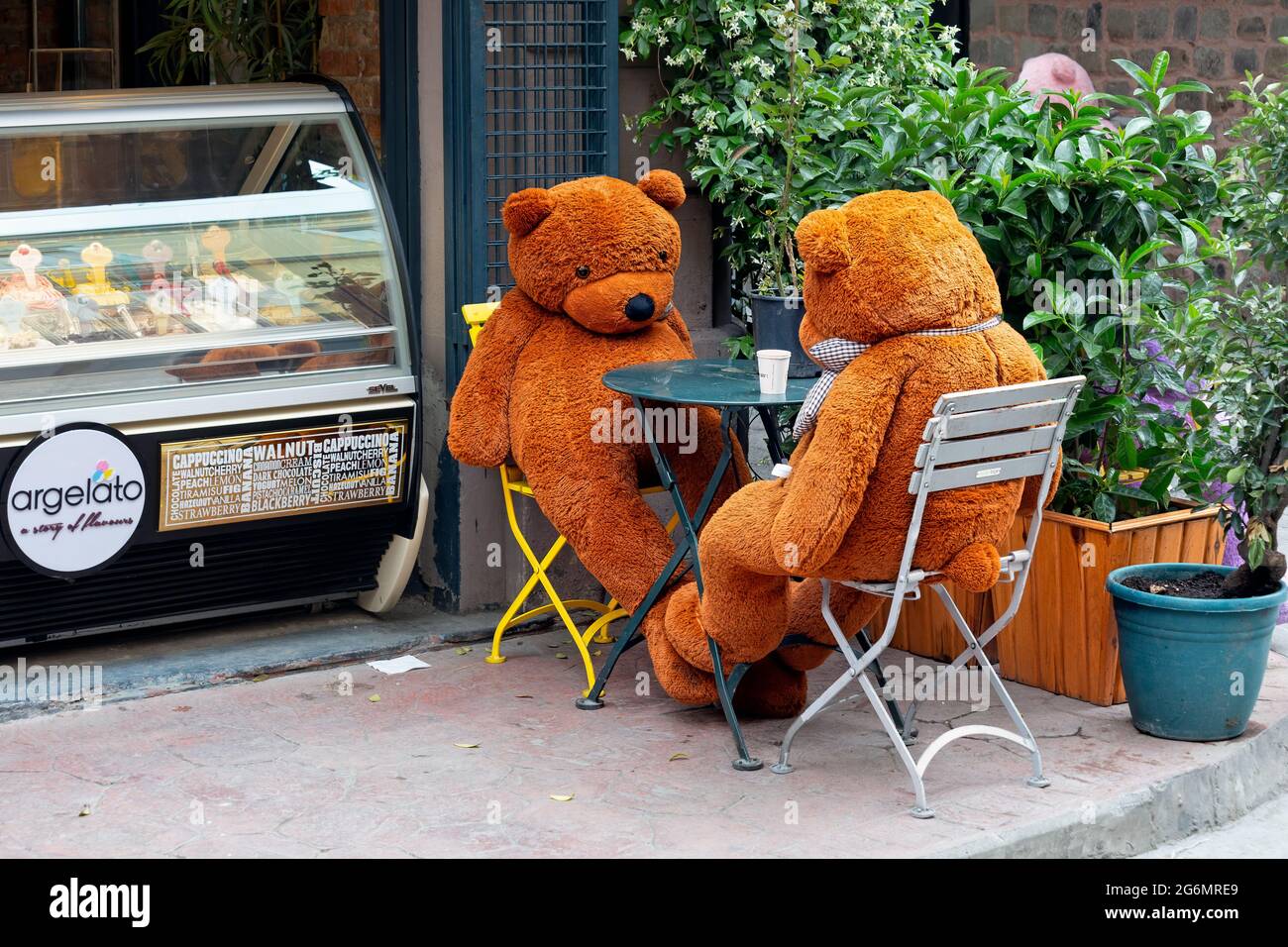 Big brown teddy bears sitting around a table of a sidewalk café and waiting to be served. Ice cream freezer in the background. Stock Photo