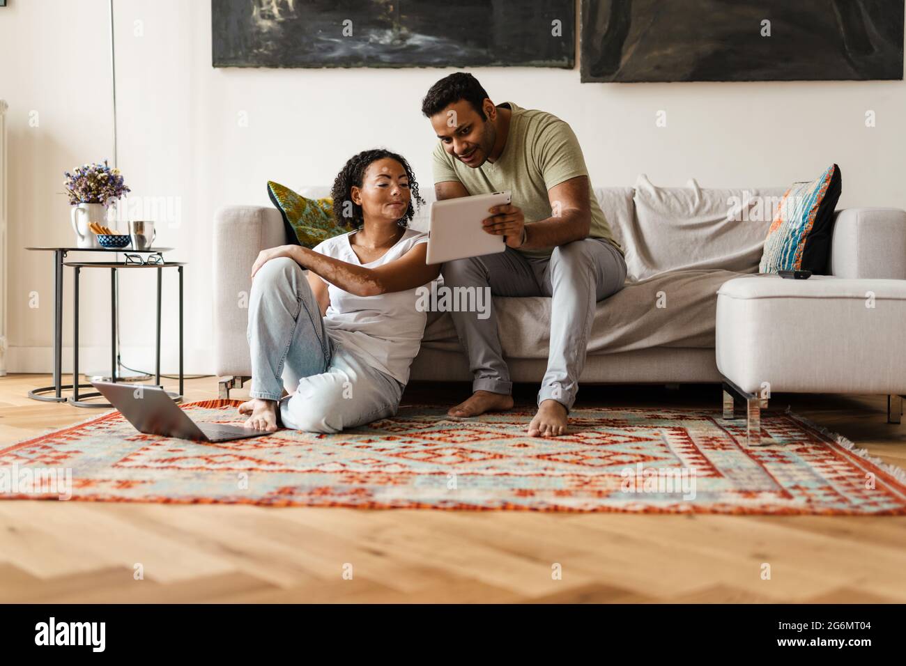 Middle eastern man and woman talking while using tablet computer and laptop at home Stock Photo