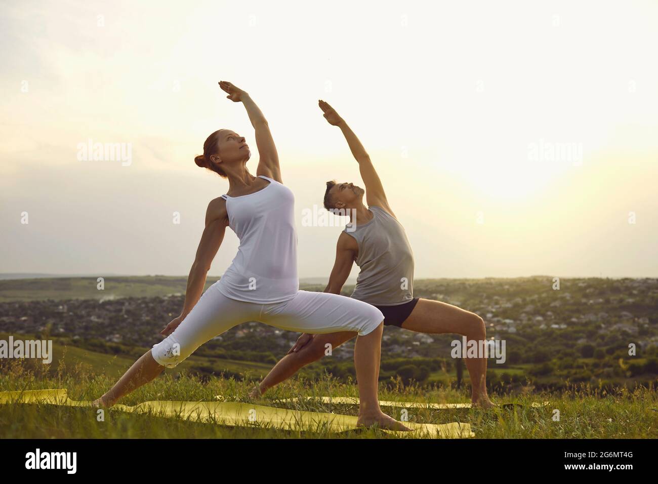 Fit man and woman in fitness clothes doing yoga together in nature in summertime Stock Photo