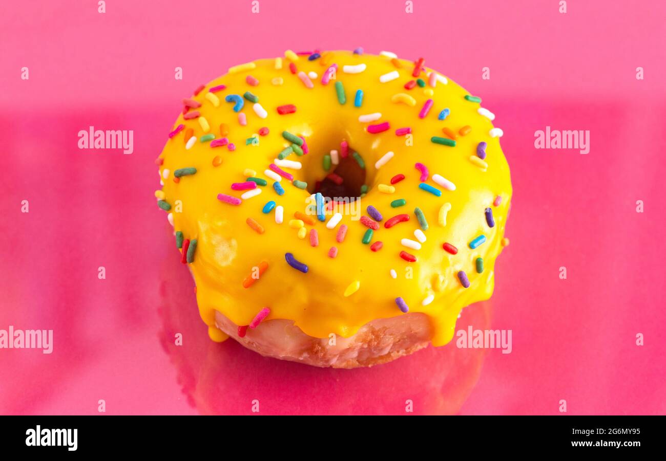 A Yellow Sprinkle Donut on a Pink Background Stock Photo