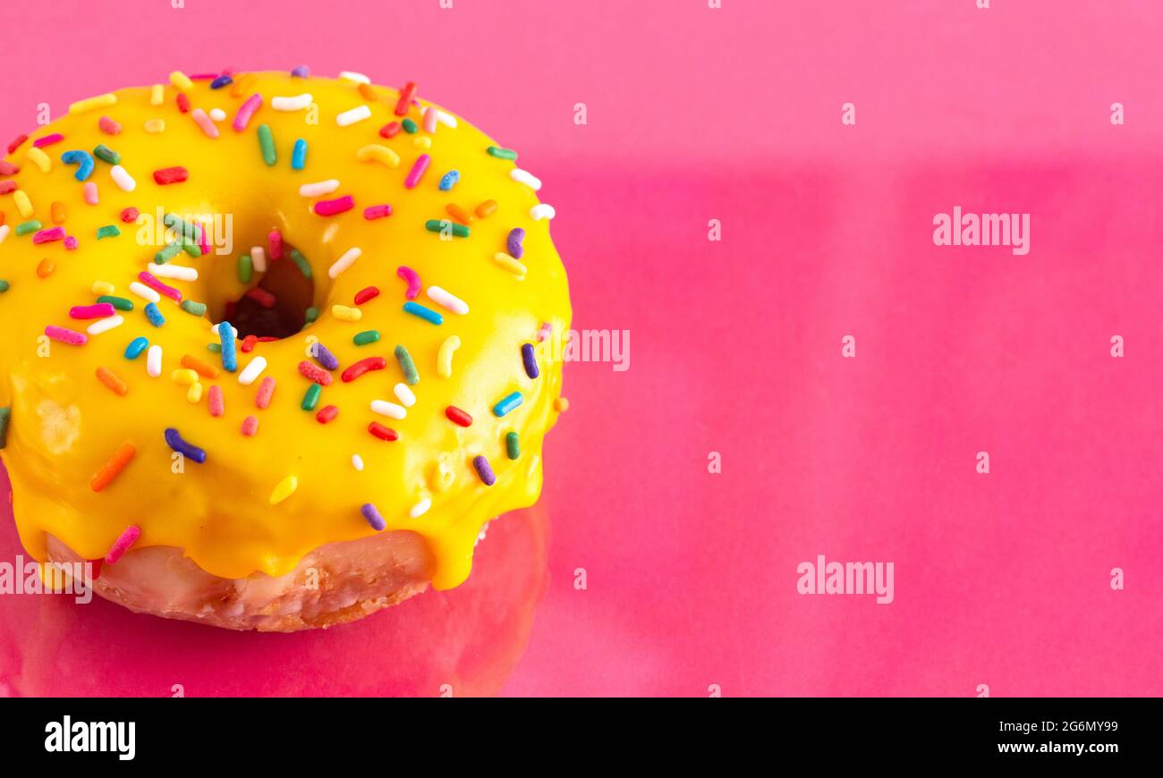 A Yellow Sprinkle Donut on a Pink Background Stock Photo