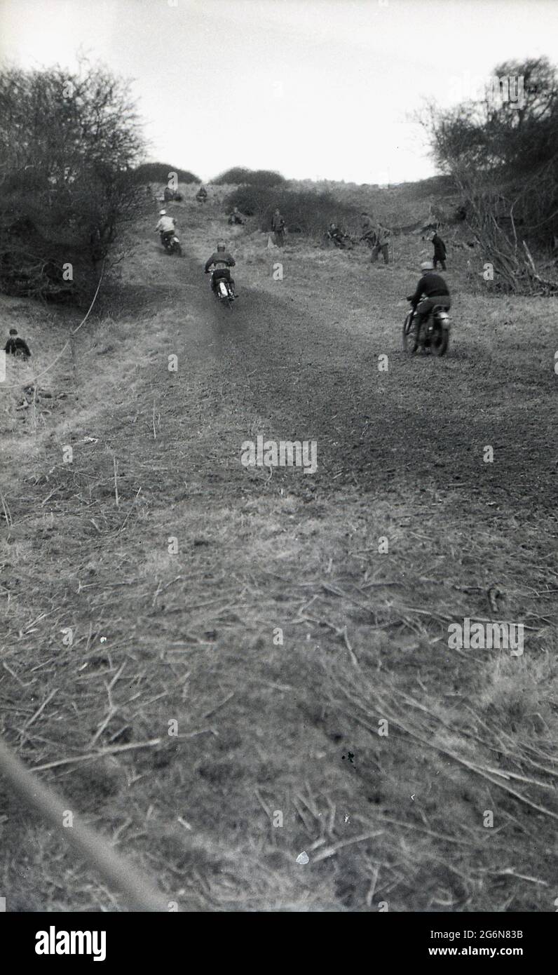 1950s, historical, scrambling, England, UK, competitors on motorcycles riding up a hill. A popular winter sport in Britan in the '50s & '60s, motorcycle scramble events were shown on BBC's Grandstand. An outside sport, ridden on natural tracks and trails, scrambling was invented in England in 1924, in Camberley. In those days, the motorbikes were little different from the road bikes of the time, with very little suspension travel. Today, the sport has evolved into motorcross, the French name for cross-country motorcycling and is known as Supercross in the USA. Stock Photo