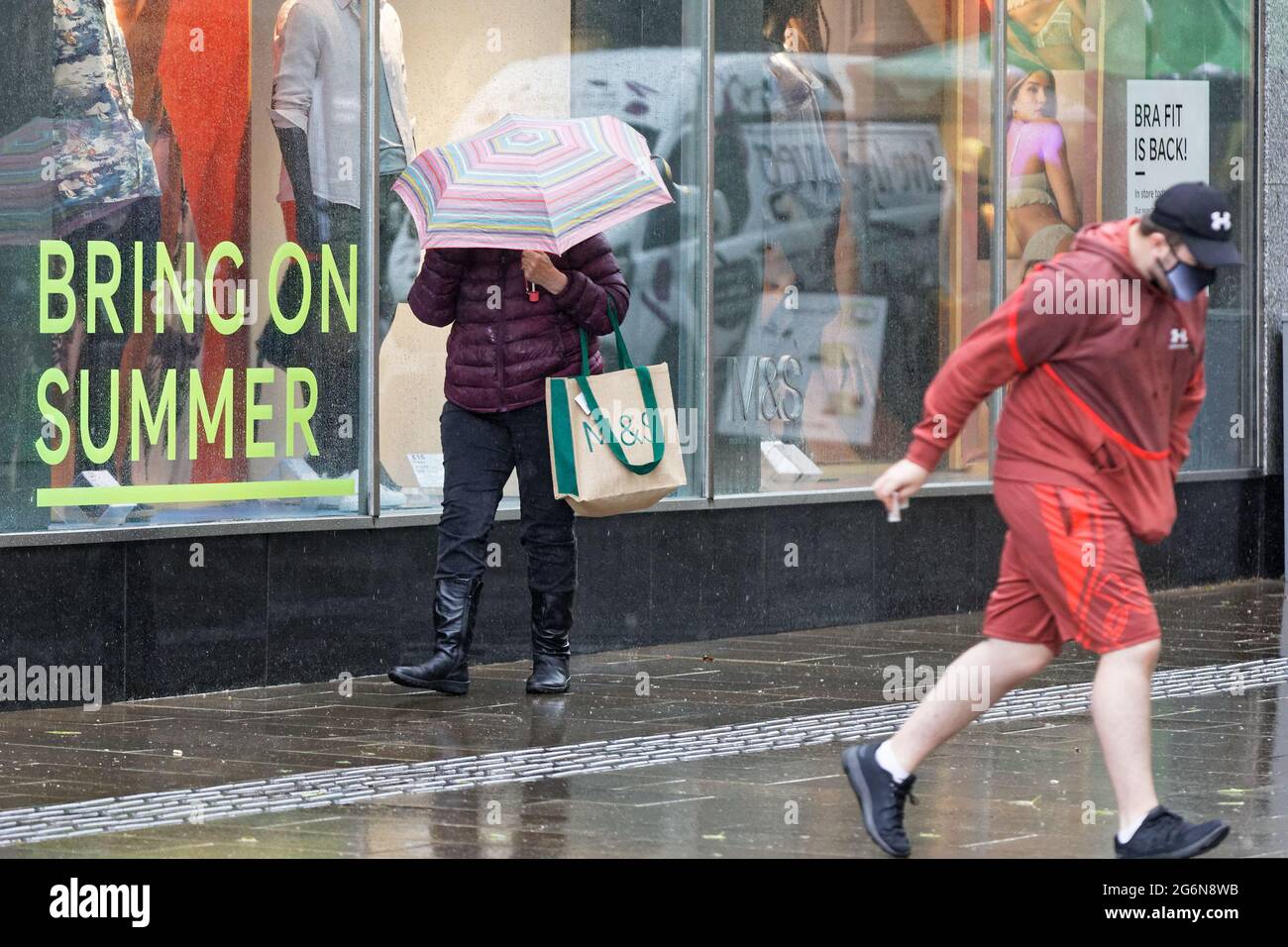 Pictured: A shopper with an umbrella, walks past a 'Bring On Summer' shop window outside the Marks and Spencer store, Oxford Street, Swansea, Wales, U Stock Photo