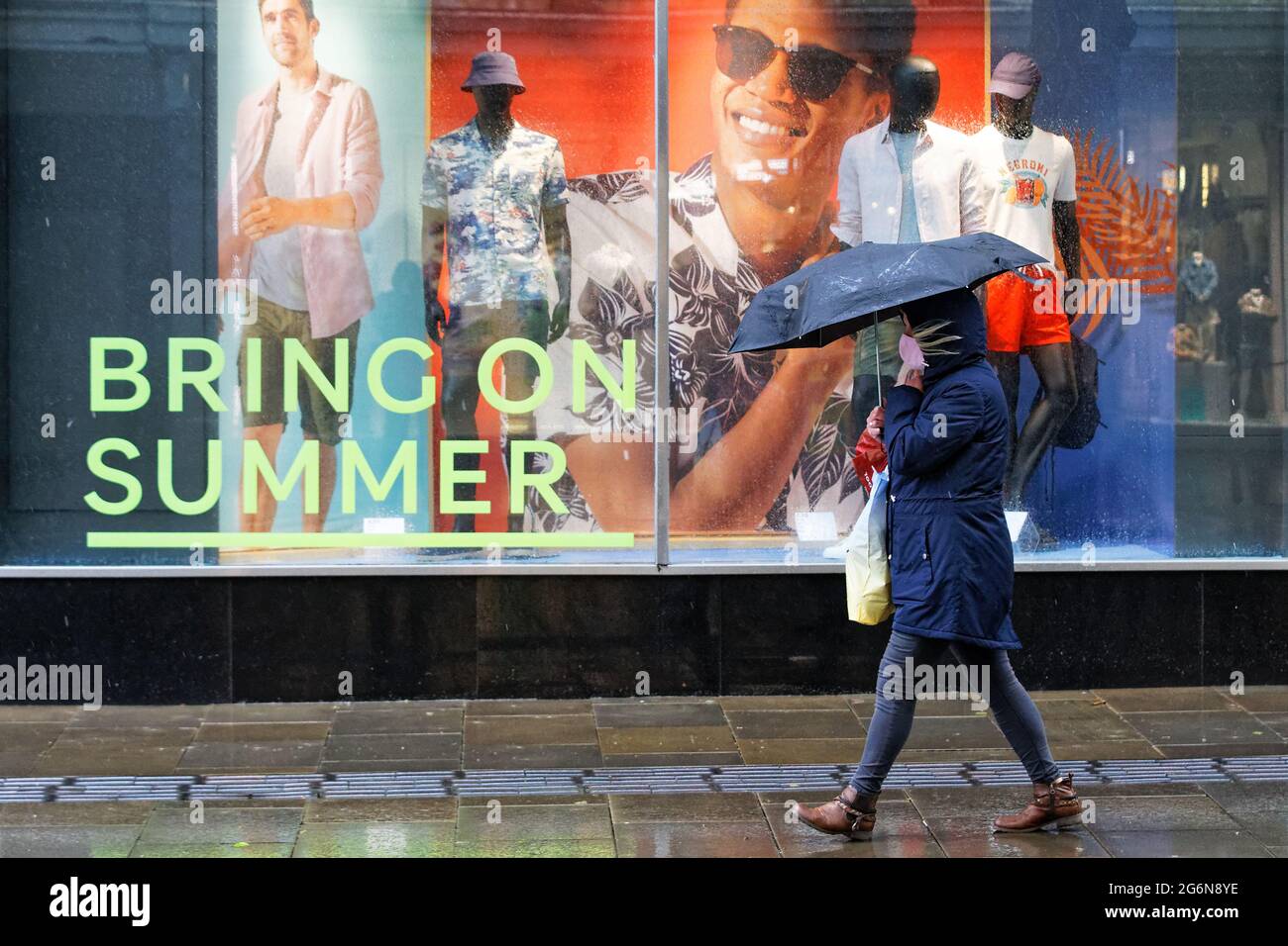 Pictured A shopper with an umbrella, walks past a "Bring On Summer