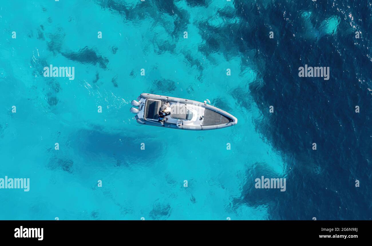 Inflatable rib speed boat on turquoise blue color sea background. Aerial drone top down view. Motorboat cruising slowly on rippled water. Aegean Sea, Stock Photo