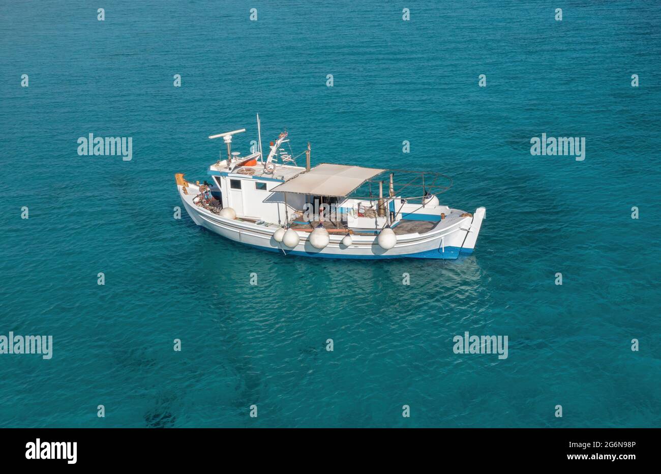 Fishing boat on turquoise blue color sea background. Aerial drone view. Blue and white traditional trawler moored in Aegean rippled water, sunny day. Stock Photo