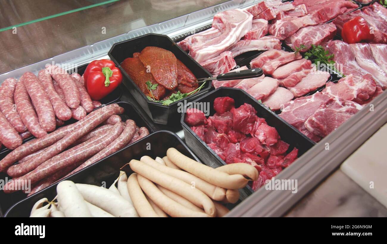 meat department display shelves with selection of typical fresh raw meats slices and variety of sausage products inside market or supermarket refriger Stock Photo