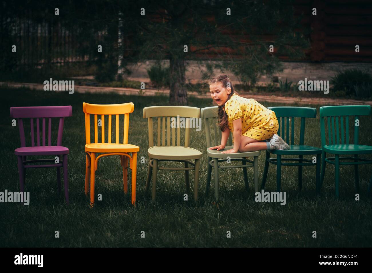 a frightened girl climbed with her feet on chairs and screams in horror after seeing something terrible in the grass in the backyard in the village Stock Photo