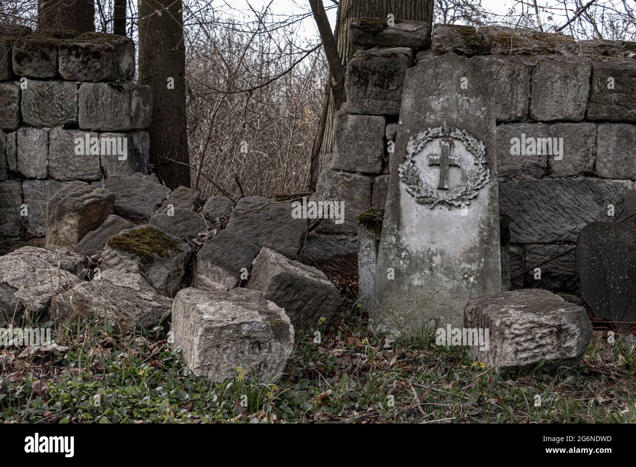 A demolished stone wall with a damaged tombstone in a cemetery Stock Photo