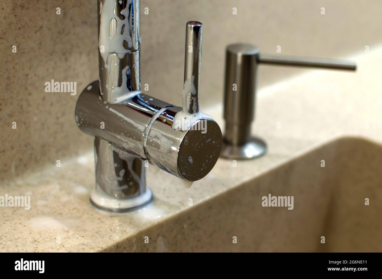 A chrome plated faucet sprinkled with cleaning agent in a new modern kitchen. Liquid soap
