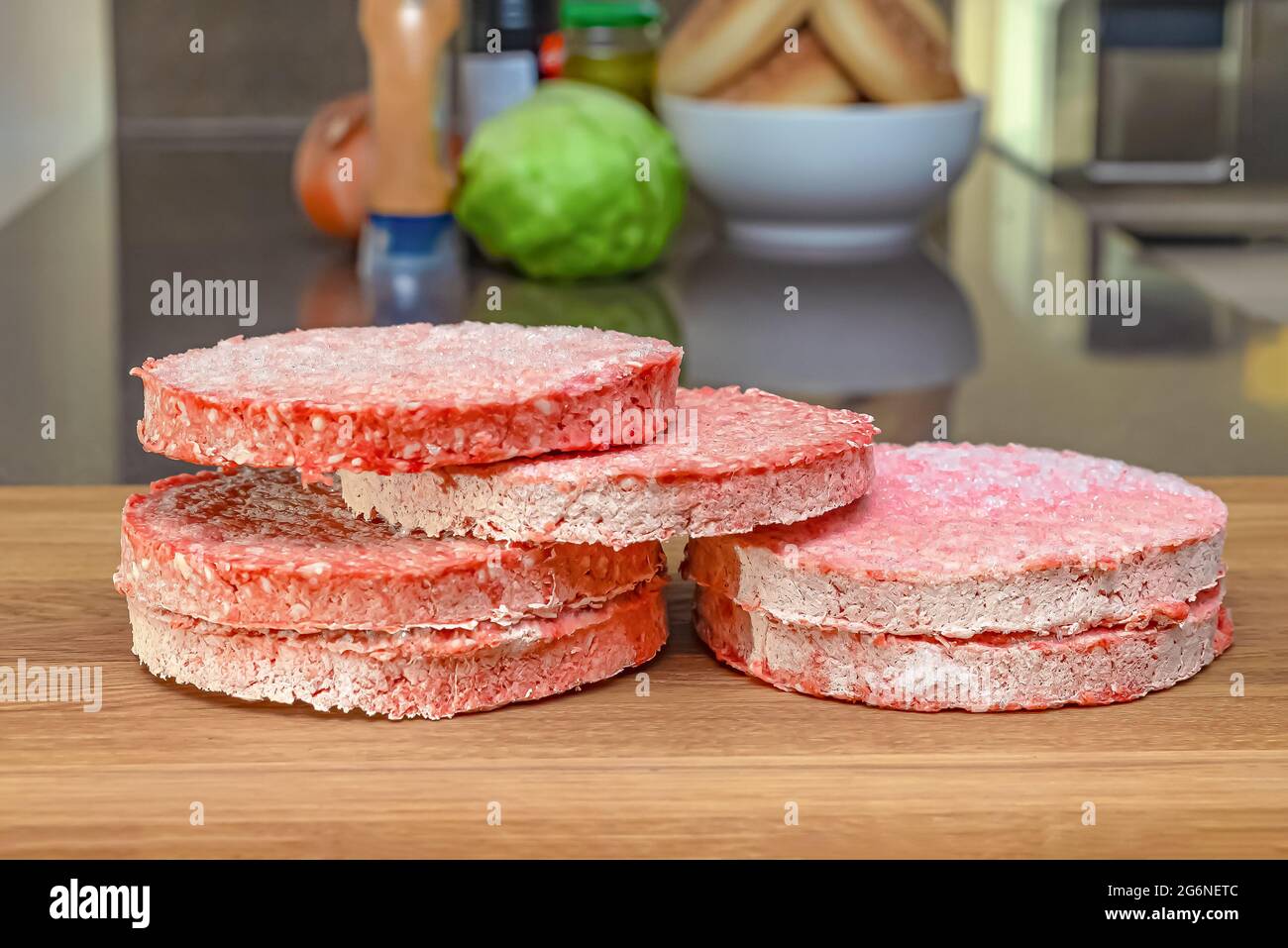 Frozen beef burger patties are placed on a wooden cutting board before