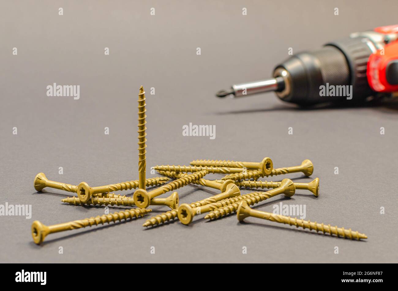Self-tapping screws on the background of a battery screwdriver, a selection of different self-tapping screws on a black background. Stock Photo