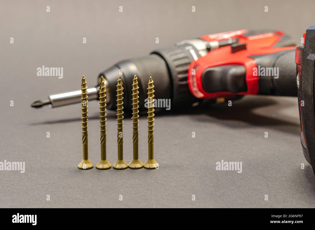 Self-tapping screws on the background of a battery screwdriver, a selection of different self-tapping screws on a black background. Stock Photo