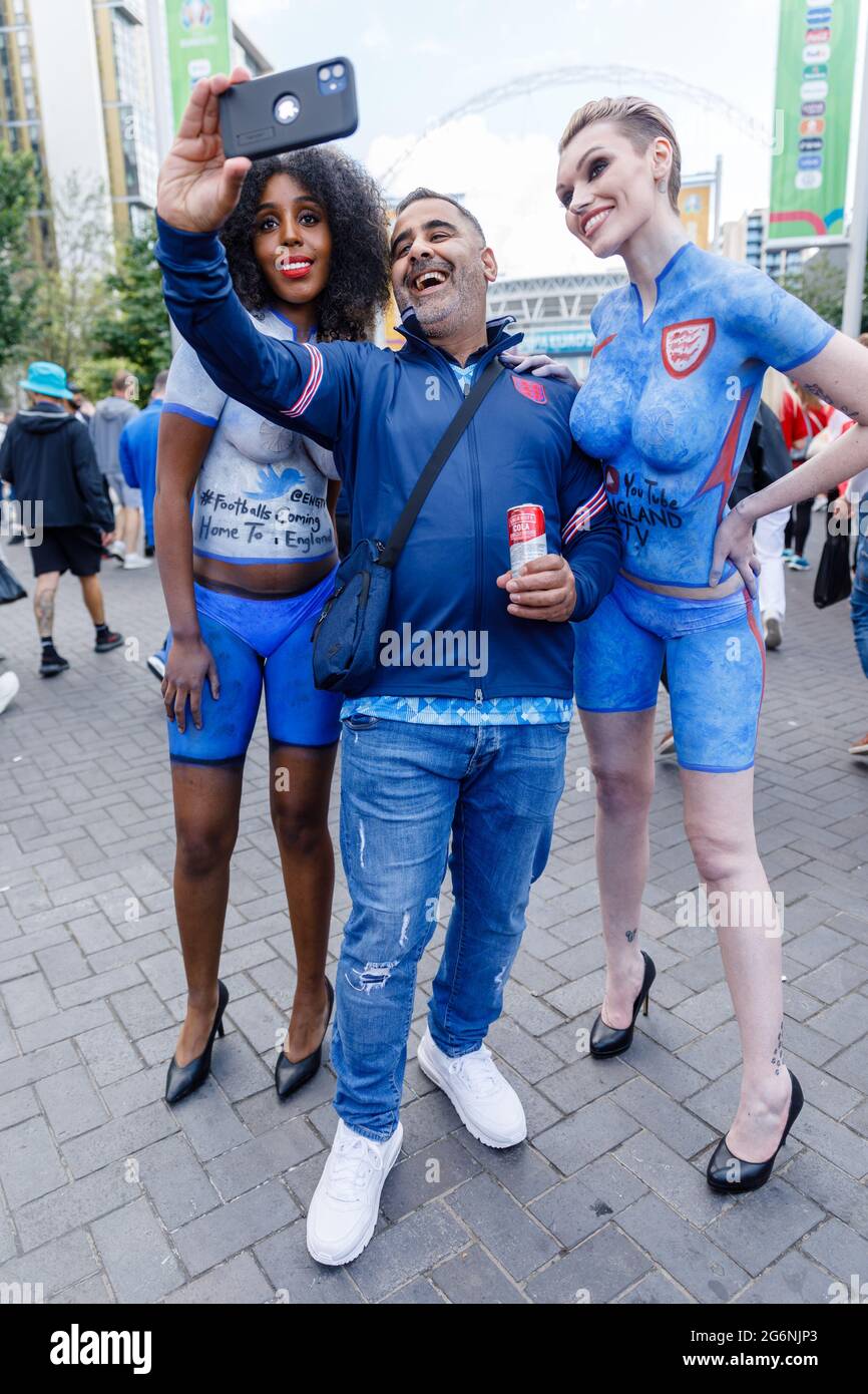 Wembley Stadium, Wembley Park, UK. 7th July 2021. 2 ladies wearing only  knickers and body paint, pose with fan on Olympic way ahead of the UEFA  EURO 2020 semi-final match at Wembley
