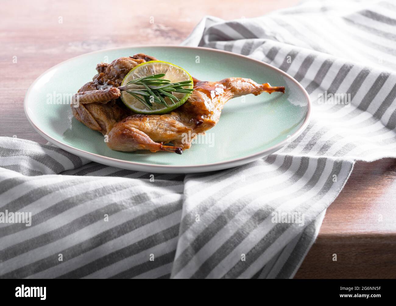 Roasted quail in a caramelised sauce with rosemary and lime on a plate. Chicken tobacco in rustic style for your meat menu on the lunch or dinner. Stock Photo