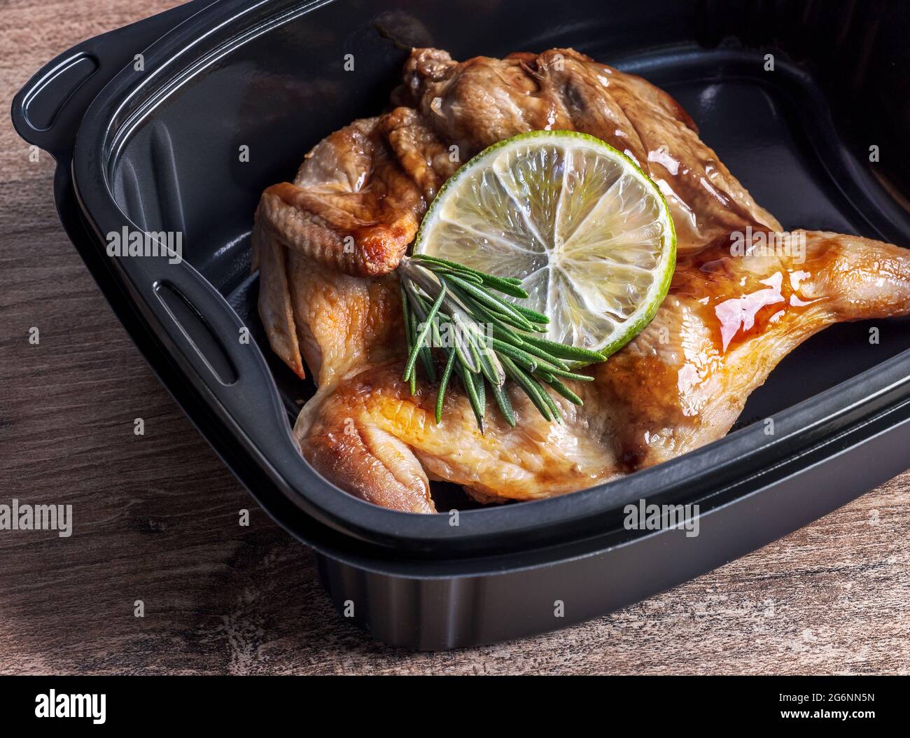 Roasted meat of a whole quail in a microwavable container, top view. Hot meal takeaway food service to home in a restaurant. Stock Photo