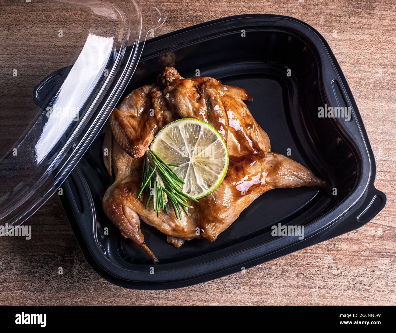 Roasted meat of a whole quail in a plastic container, top view. Hot meal takeaway food service to home in a restaurant. Stock Photo