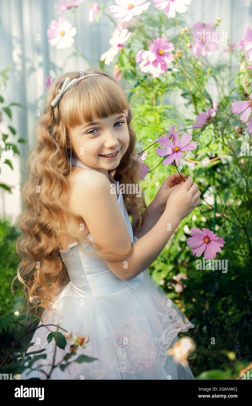 Portrait of a 10-year-old little girl in a blooming rose garden. Cute beautiful cute baby having fun with flowers in the park on a sunny summer day. h Stock Photo