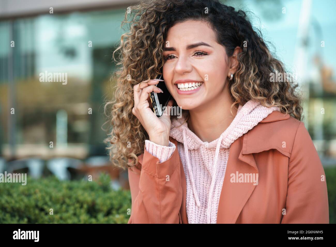Latin woman smiling while talking on the phone outdoors in the street ...