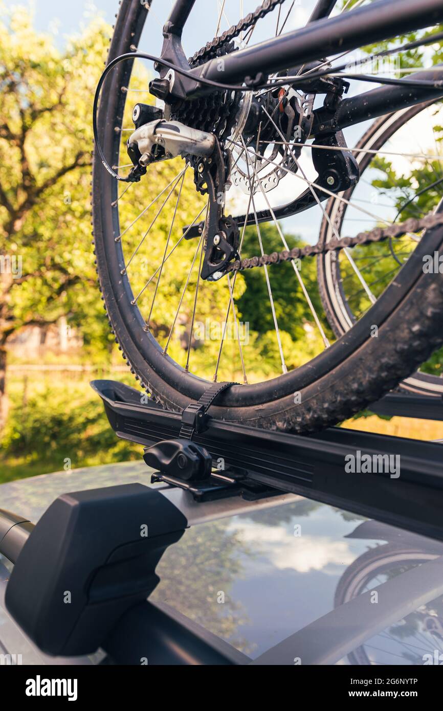 Bicycle installed to roof bike rack on a silver car, coutryside landscape in background Stock Photo