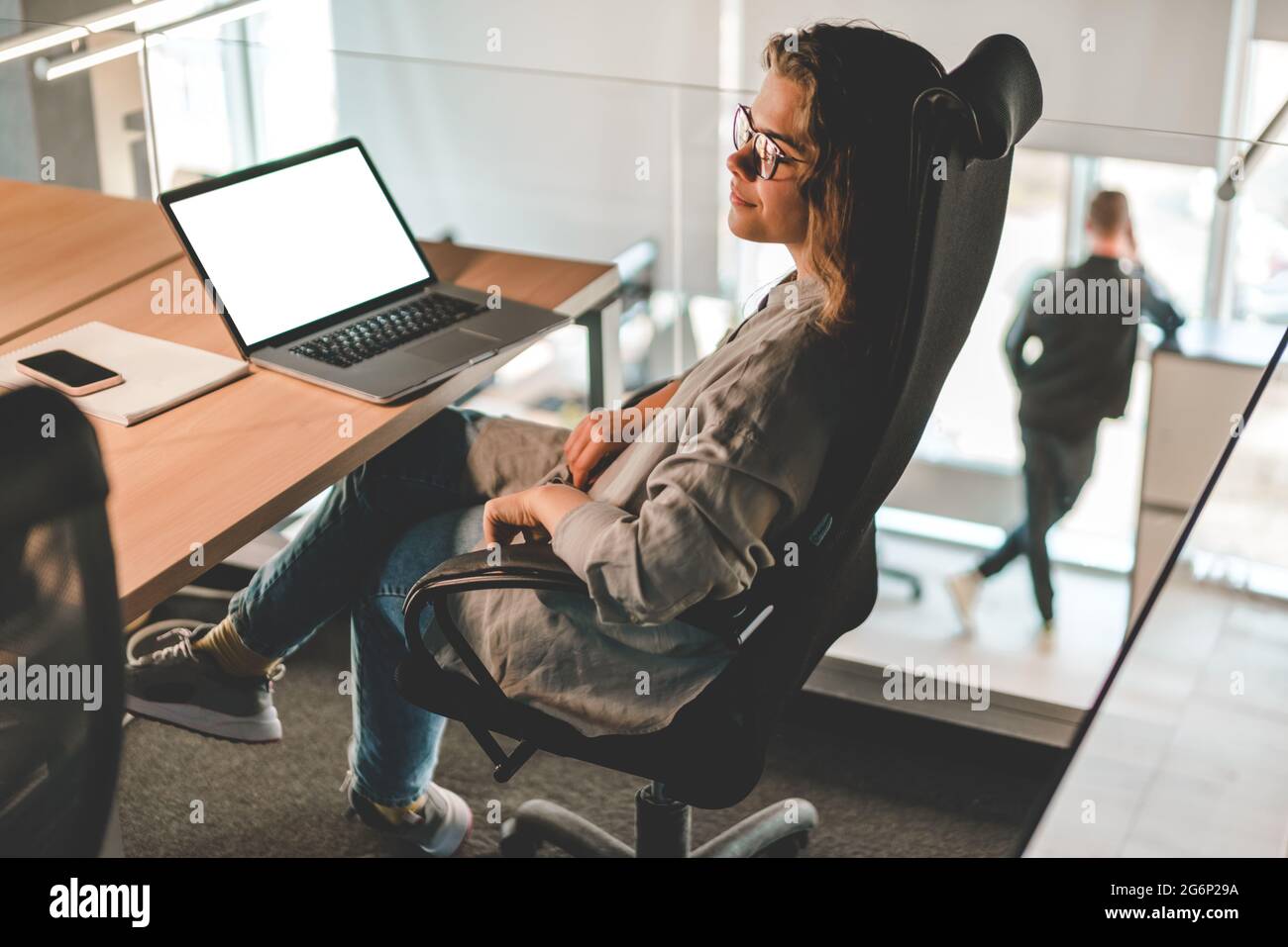 Young woman in glasses sitting in the office, thinking, laptop at her workplace. Modern communication technology, remote working and freelance job Stock Photo