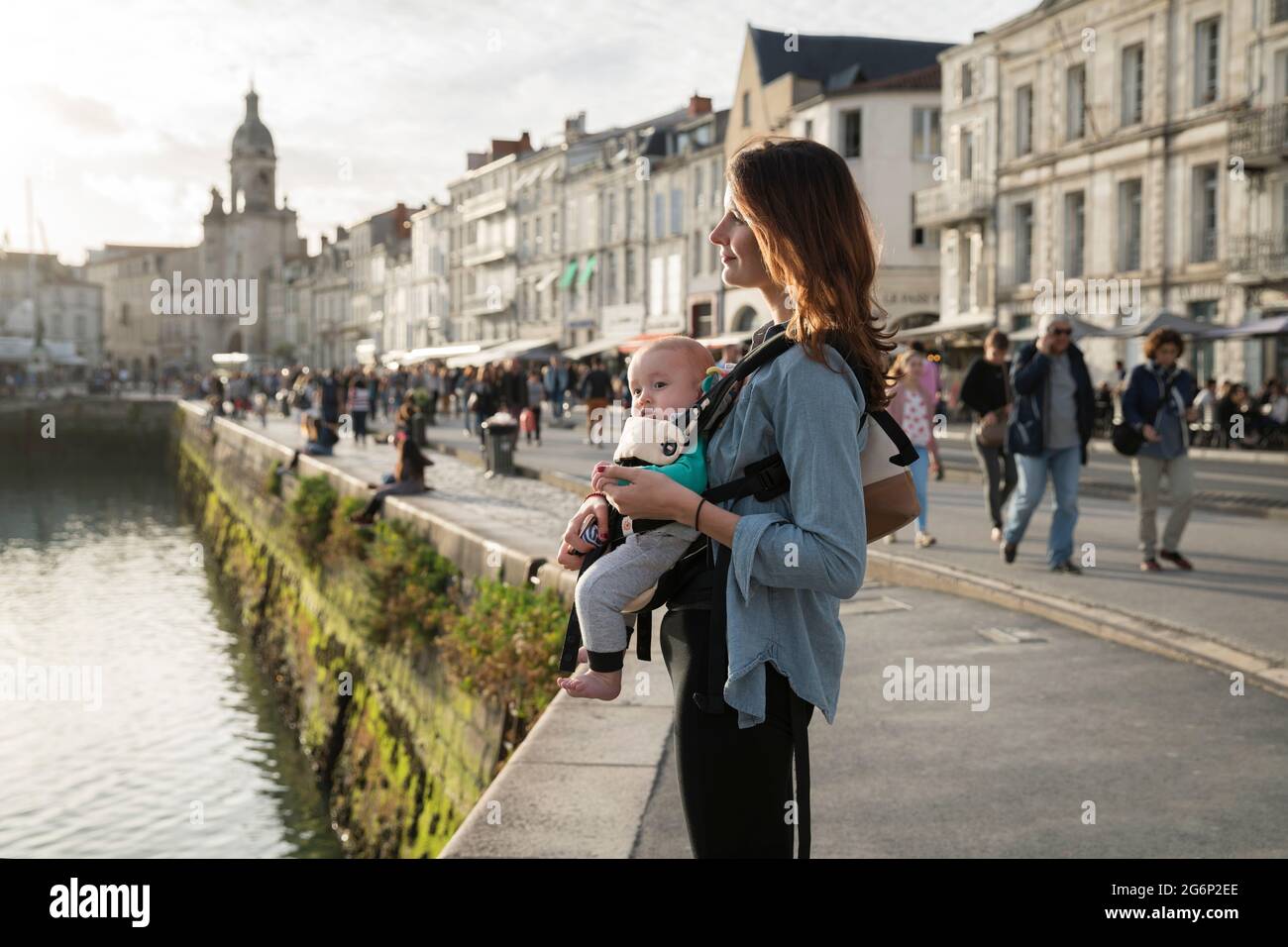 A woman walking with her baby in a sling in La Rochelle, France Stock Photo
