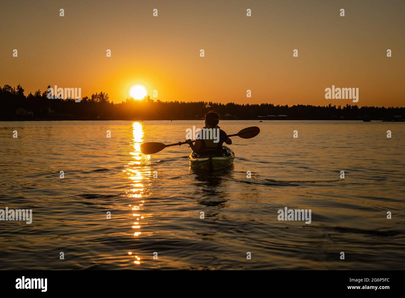 Girl kayaking and taking pause calm sea at midnight in Northern Sweden during light Summer nights. All day around Sun in polar regions. Stock Photo