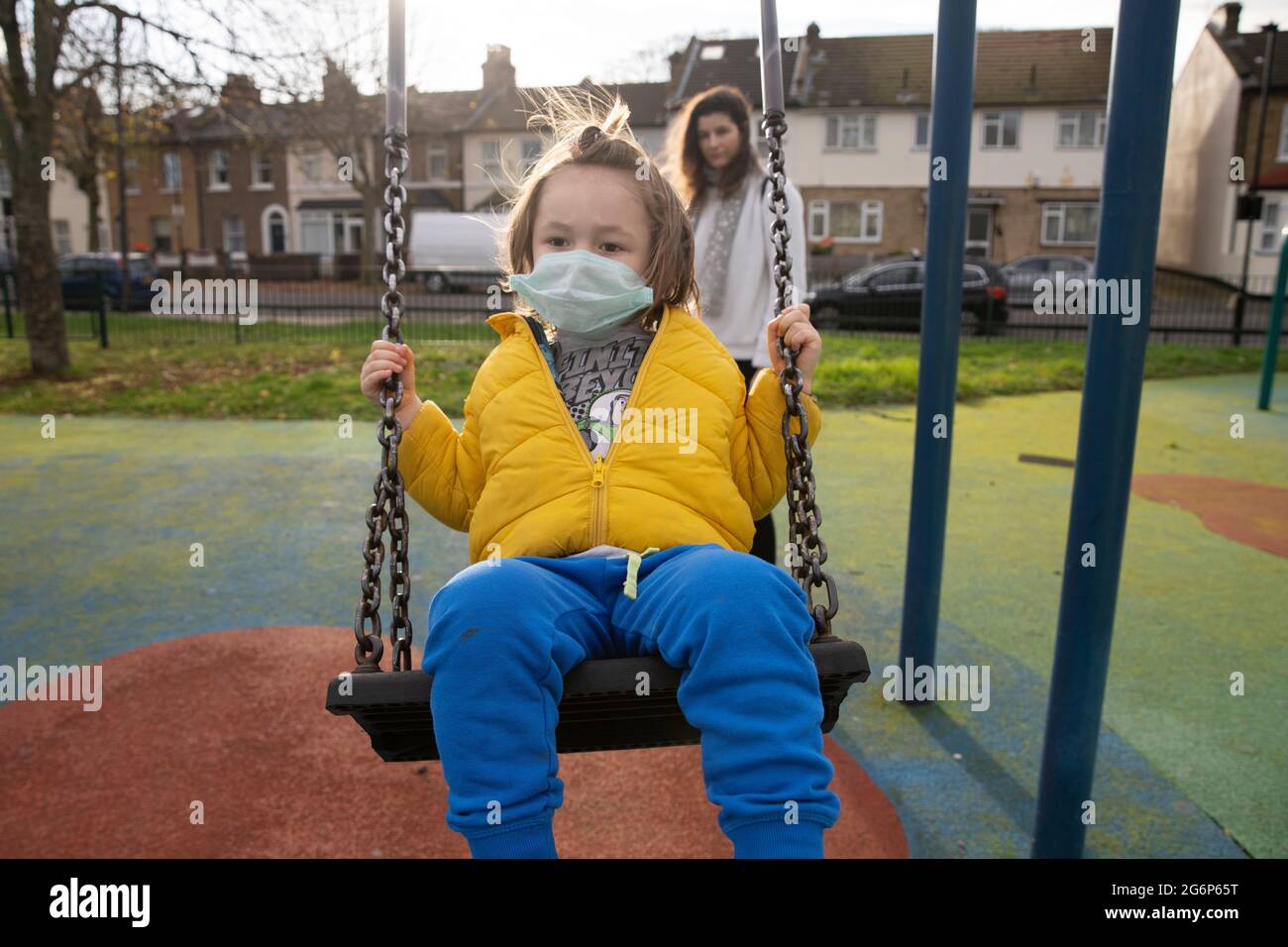 A child in a mask being pushed on a swing by his mother Stock Photo