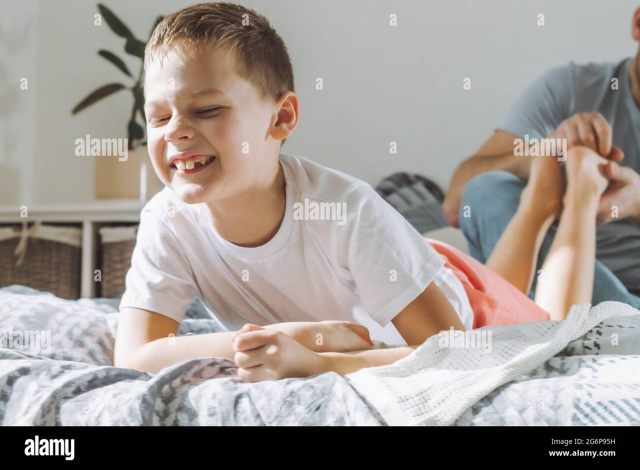 Father plays with his son 7-10 on bed. Dad tickles kids feet. Family having fun Stock Photo