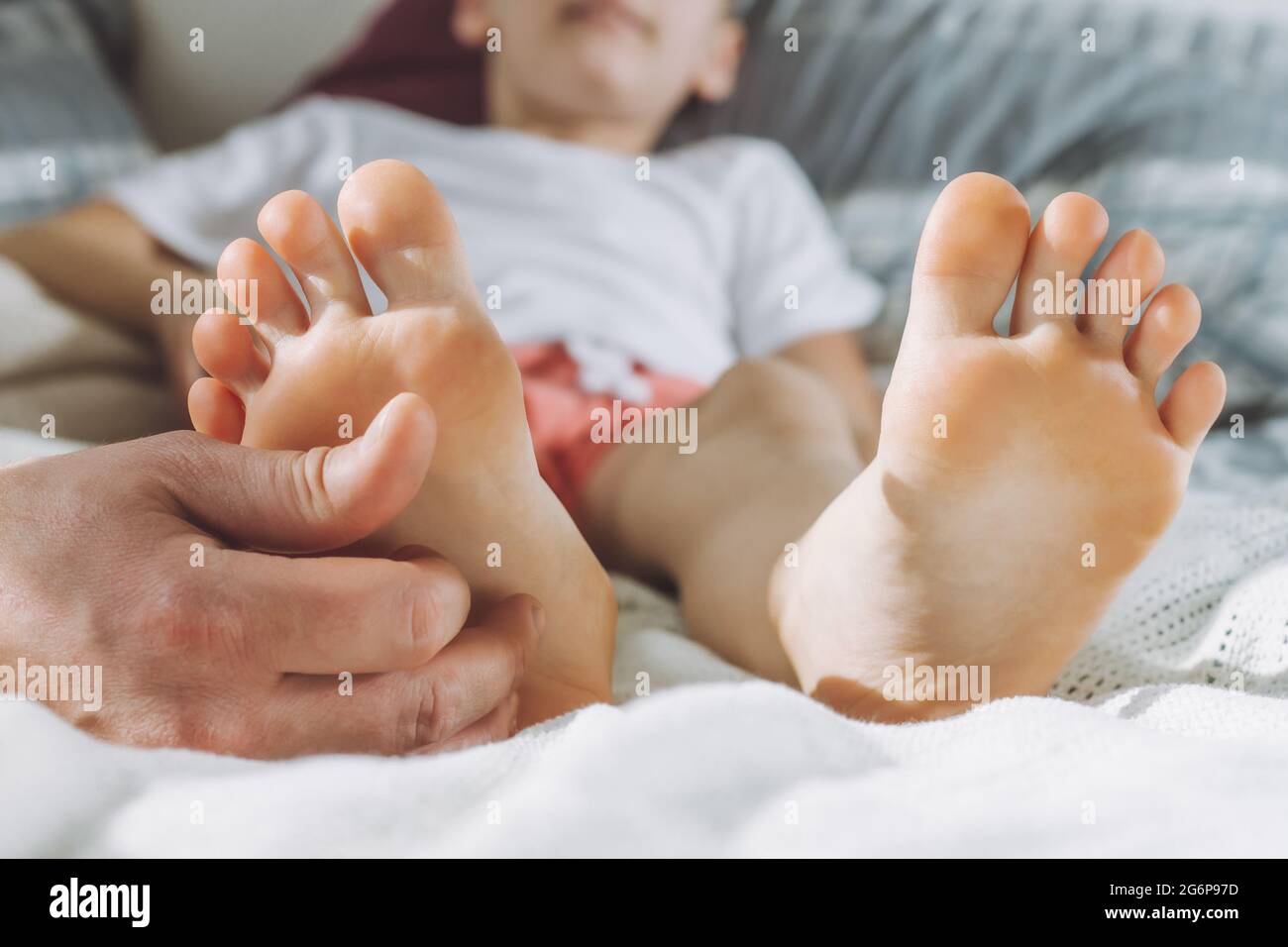 Dad tickles feet of kid. Boy lies on bed and plays with his father. Family having fun at home Stock Photo