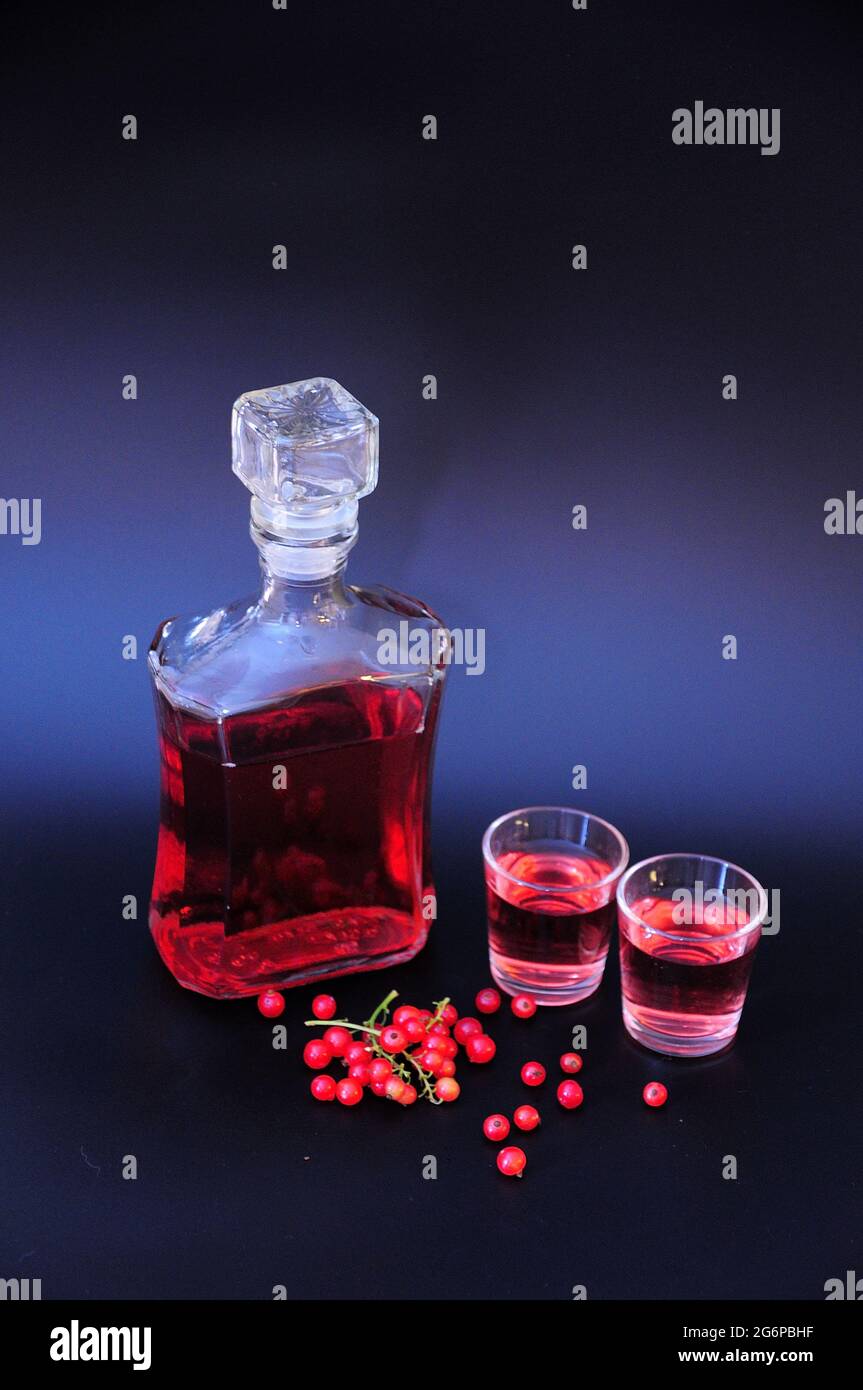 Homemade red currant liqueur and bunches of ripe berries next to two