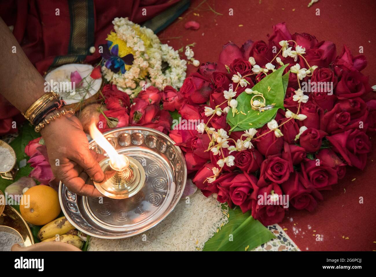 Hand holding a burning candle placed on the rice grains surrounded by ...