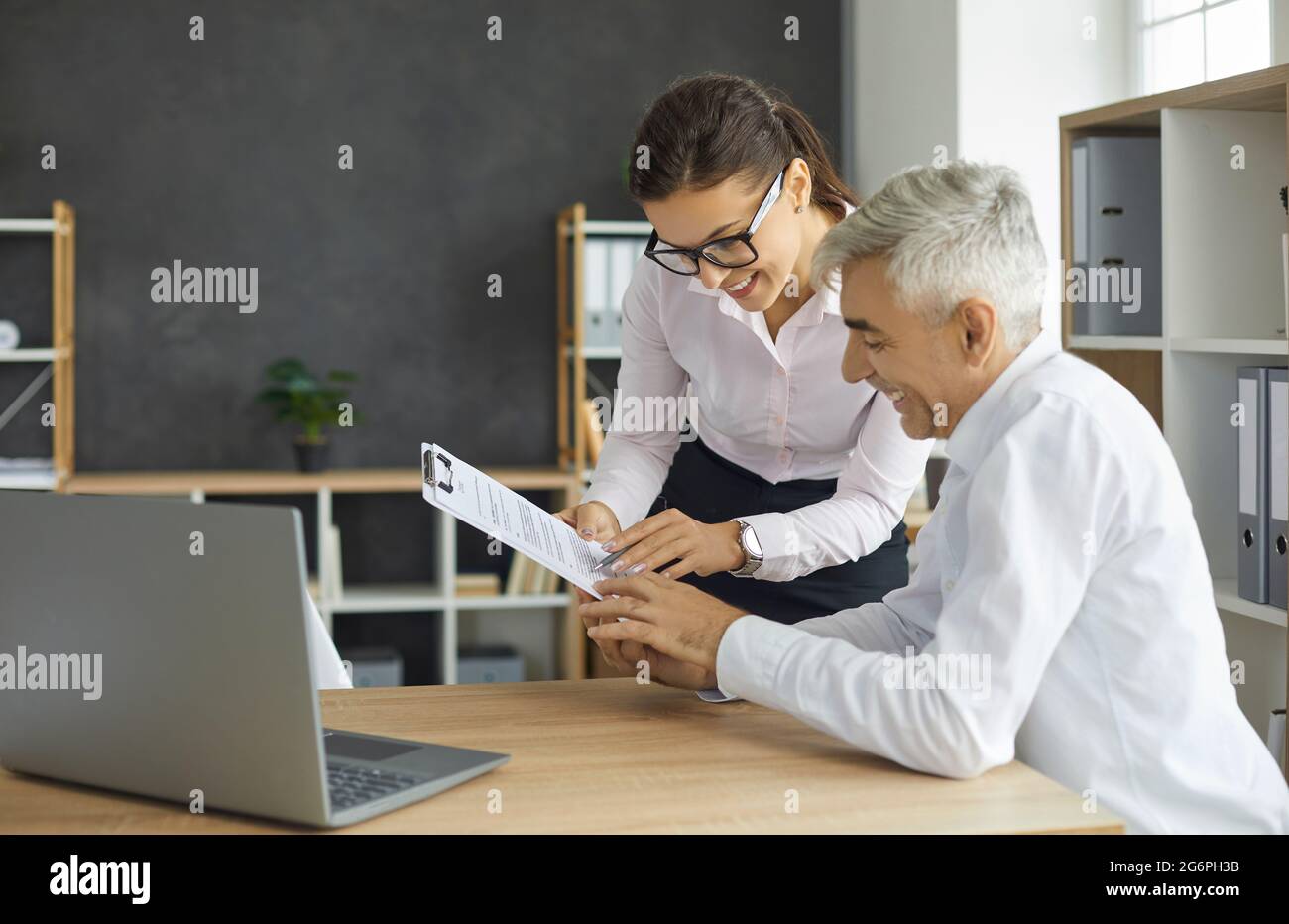 Smiling female secretary gives her senior manager paper documents or a contract to sign. Stock Photo