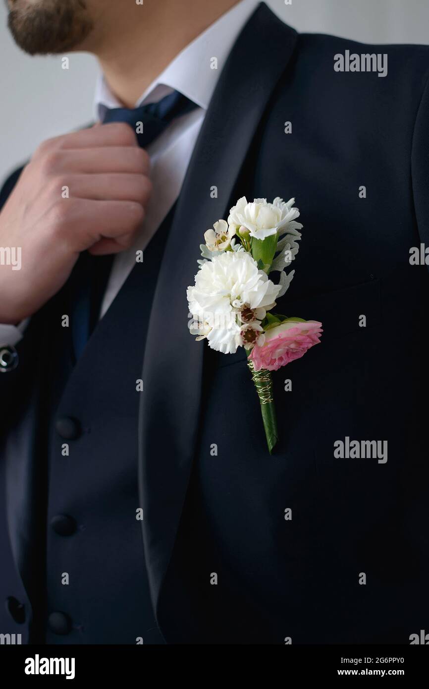 Groom in a dark blue suit with a boutonniere adjusts his tie looking to the side in close-up Stock Photo