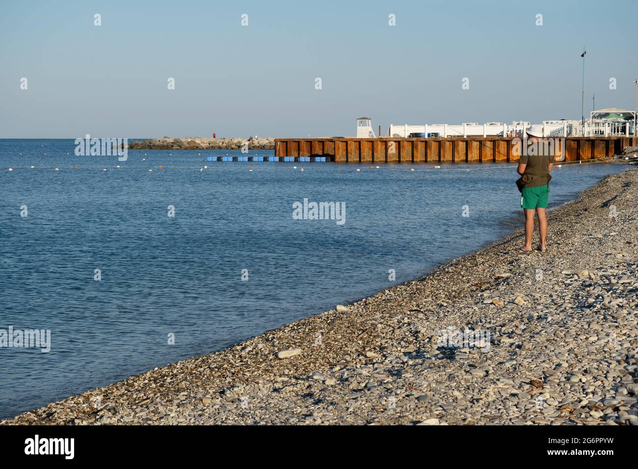 A sea scene of the back view of a man fishing from the pebble beach in the bay of the resort village of Nebug, Krasnodar Territory, Russia. Stock Photo
