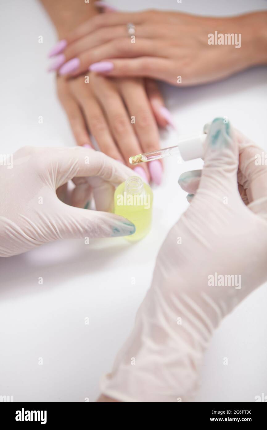 Vertical shot of a nail technician applying cuticle oil on hands of