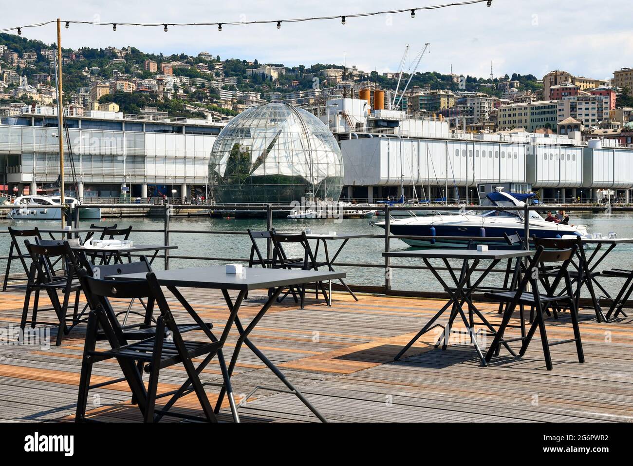 An empty outdoor restaurant on the waterside of the Old Port with the Biosphere and the Aquarium in the background, Genoa, Liguria, Italy Stock Photo
