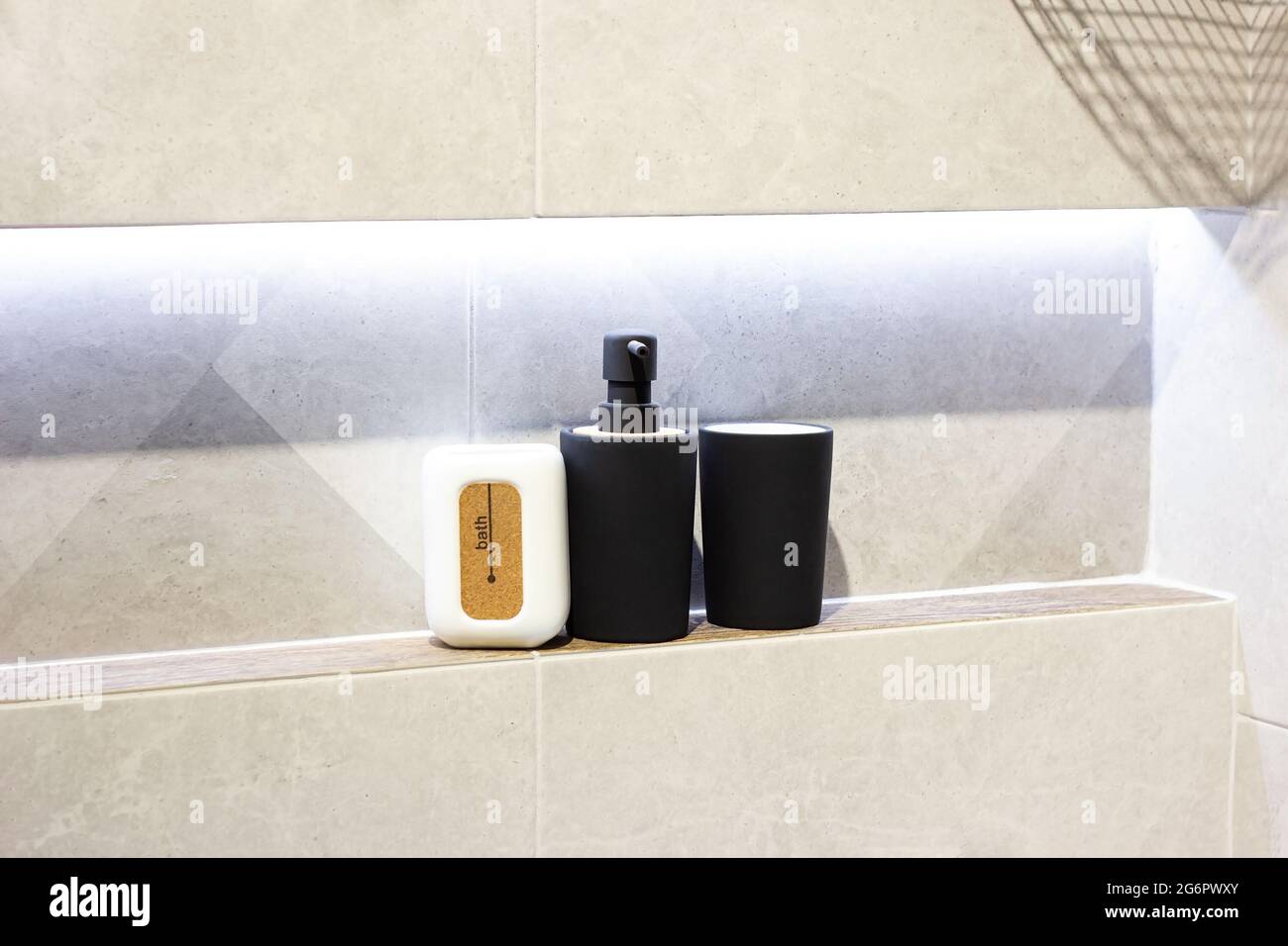 New black and white bath dispensers and bottles in the hotel bathroom on light tile wall background. Stock Photo
