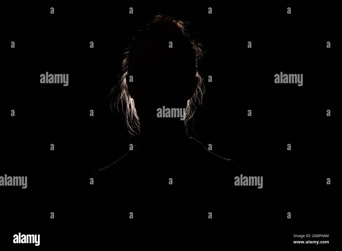 backlit portrait silhouette of unrecognizable woman hiding face and identy in the dark shadow Stock Photo