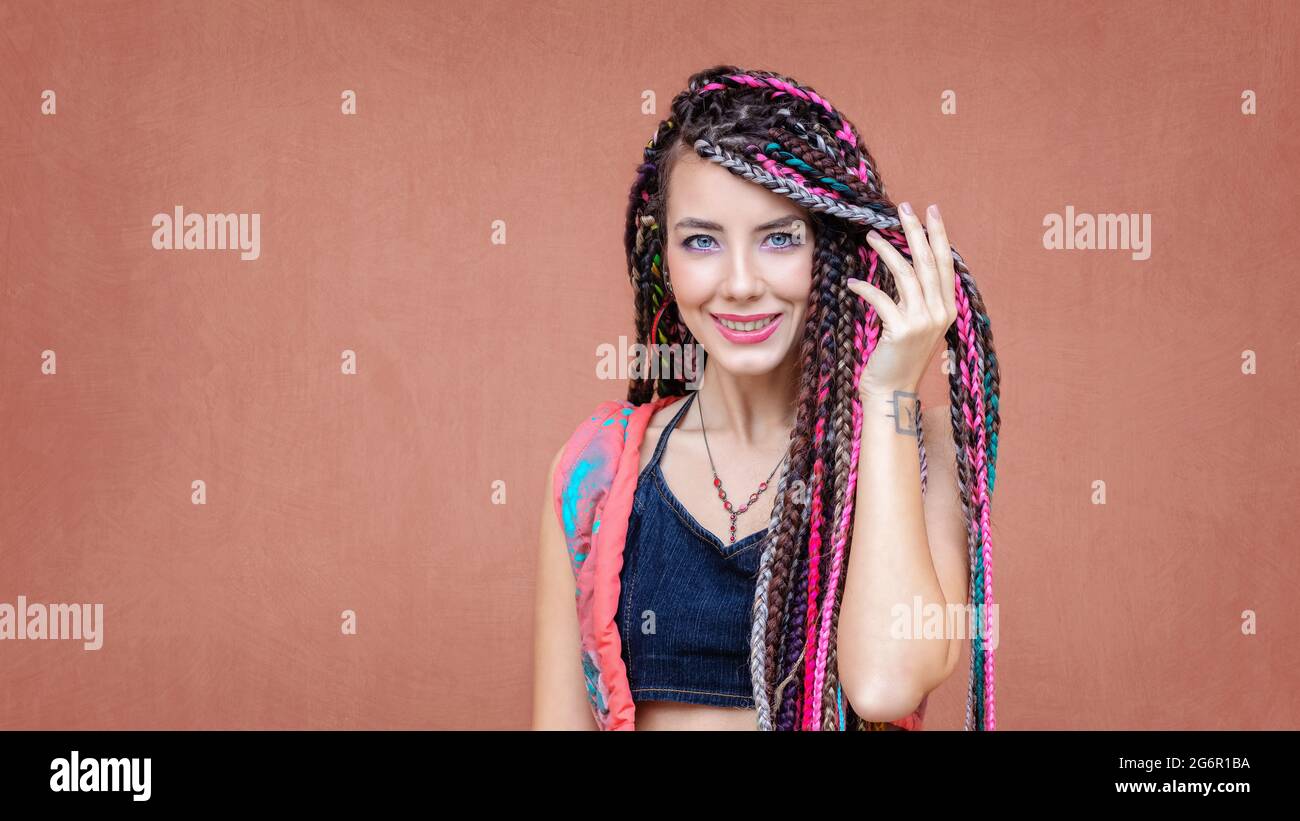 Happy hispanic girl with braids and tattoo smiling at camera outdoors with colorful background Stock Photo