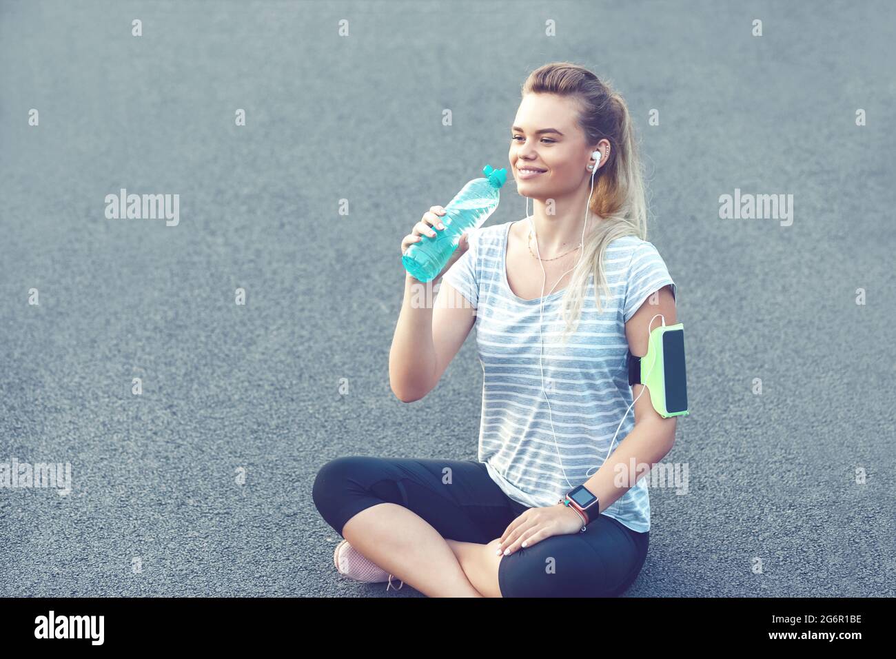 Happy young sporty woman drinking water from bottle while taking a break after running workout Stock Photo