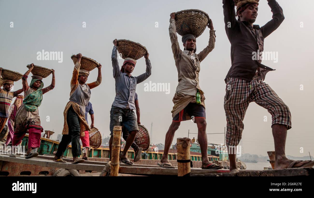 A human chain of porters carry coal, sand and gravel from the barges that are moored at the Aminbazar Landing Station on the Buriganga River outside Dhaka. Bangladesh is graduating from the LDC category (Least Developed Countries), thanks in big parts to the extremely hard work of  cheap manual labor force. A porter makes between 80 and 140 USD per month, according to the websites paylab.com and averagesalarysurvey.com Stock Photo